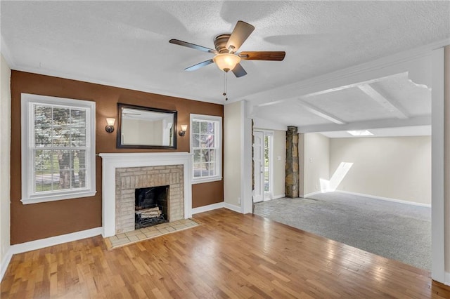unfurnished living room with baseboards, wood finished floors, a brick fireplace, and a textured ceiling