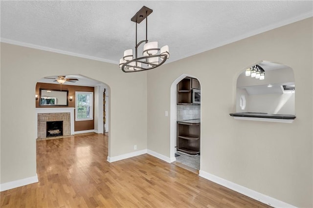 unfurnished dining area with arched walkways, wood finished floors, a textured ceiling, a fireplace, and ornamental molding
