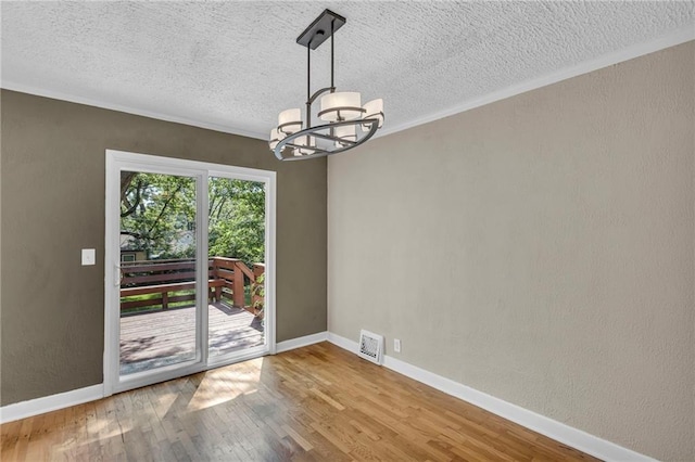 unfurnished dining area with a chandelier, a textured ceiling, wood finished floors, baseboards, and crown molding
