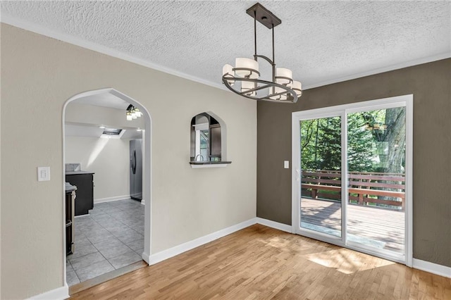 unfurnished dining area with wood finished floors, arched walkways, ornamental molding, a chandelier, and a textured ceiling