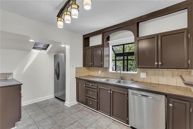 kitchen featuring appliances with stainless steel finishes, a sink, decorative backsplash, dark brown cabinets, and baseboards