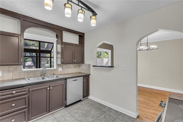kitchen featuring dishwasher, a sink, arched walkways, backsplash, and baseboards