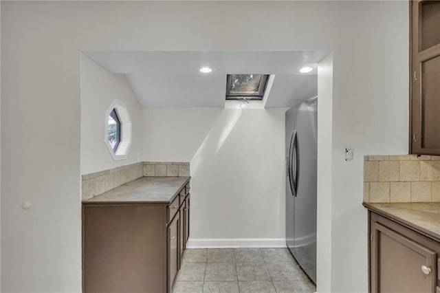 kitchen featuring stainless steel fridge with ice dispenser, light tile patterned floors, tile countertops, and baseboards