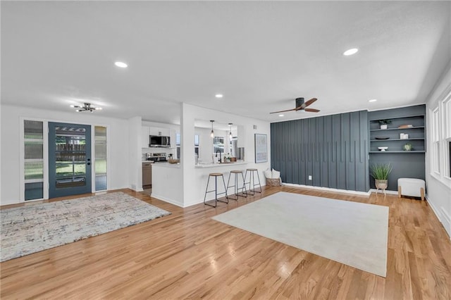 living area with ceiling fan, light wood finished floors, built in features, recessed lighting, and baseboards
