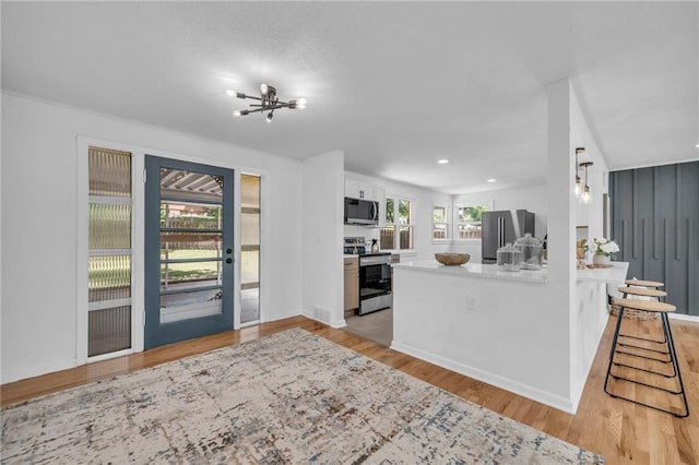 kitchen with appliances with stainless steel finishes, light wood finished floors, a chandelier, white cabinets, and a peninsula
