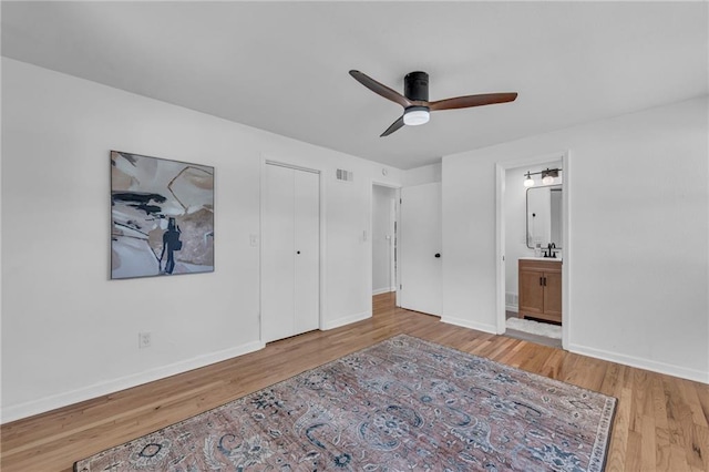 unfurnished bedroom featuring wood finished floors, baseboards, ensuite bath, and ceiling fan