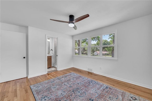 unfurnished bedroom with wood finished floors, baseboards, ensuite bath, and a ceiling fan
