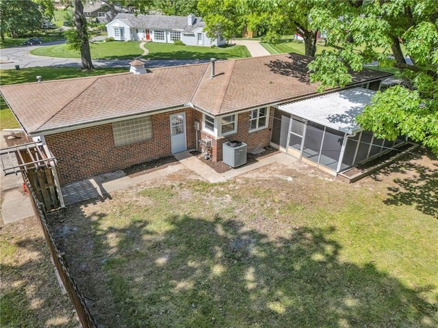 back of property with a sunroom, central AC unit, brick siding, a lawn, and roof with shingles