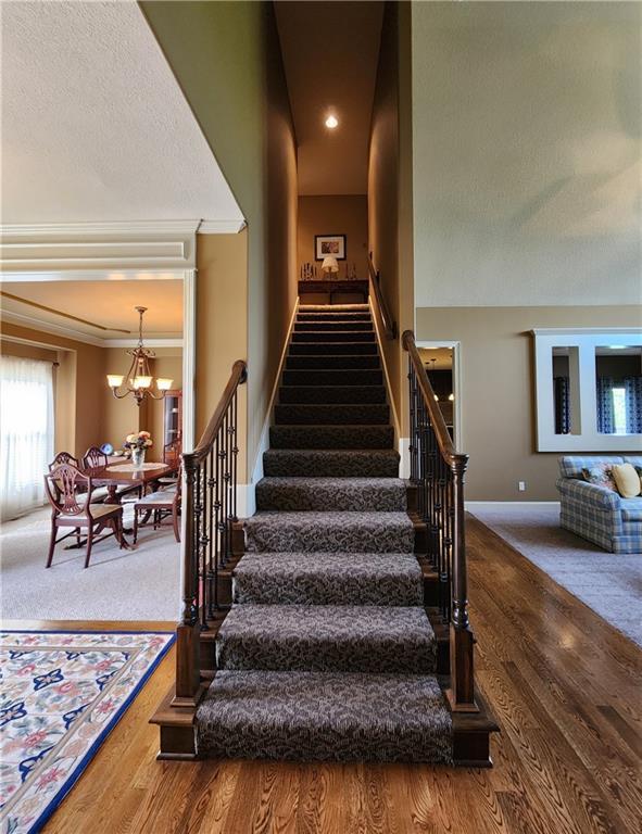 14650 NW 66th Ter, Parkville, MO 64152 - stairway featuring a chandelier, wood finished floors, baseboards, crown molding, and carpet floors