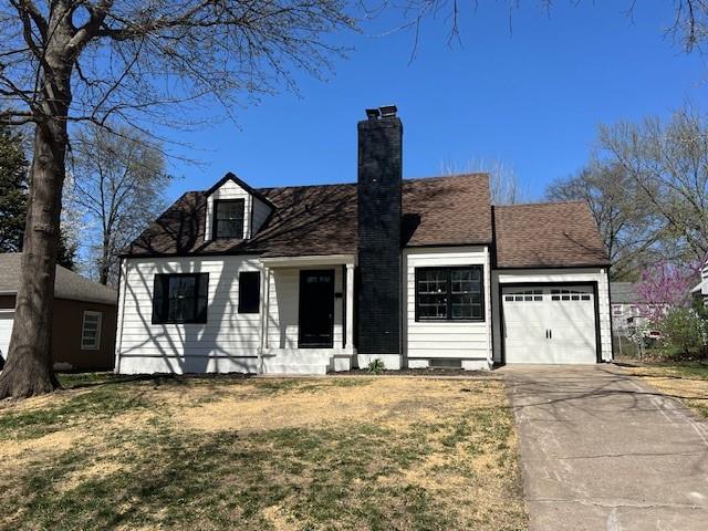 new england style home featuring an attached garage, a chimney, driveway, and a front yard