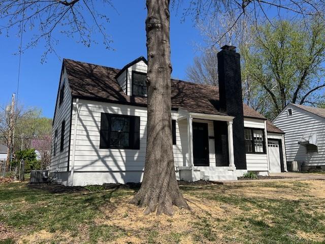 view of front of home with a chimney, a garage, a front yard, and central AC