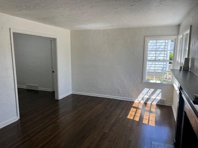 unfurnished dining area with dark wood-type flooring, a textured ceiling, baseboards, and a textured wall