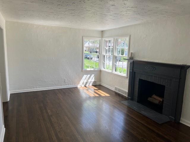 unfurnished living room with wood finished floors, a textured ceiling, a fireplace with flush hearth, a textured wall, and baseboards