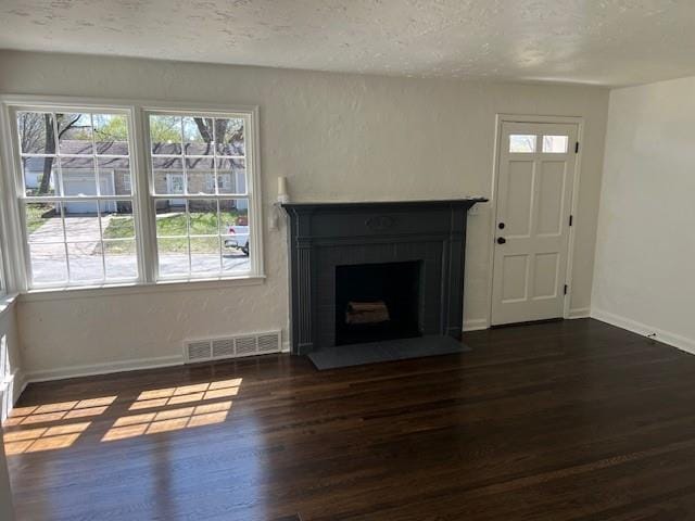 unfurnished living room with dark wood-style floors, baseboards, a fireplace with flush hearth, and a textured ceiling