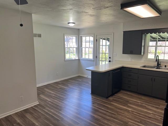 kitchen with a sink, a peninsula, baseboards, dark wood-style flooring, and light countertops