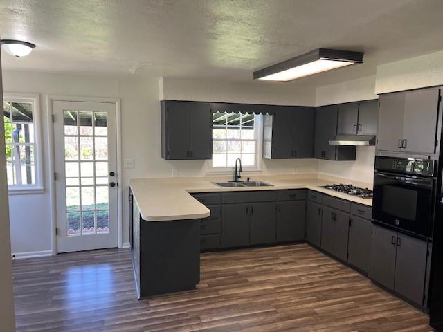 kitchen featuring oven, a sink, stainless steel gas cooktop, dark wood-type flooring, and a peninsula