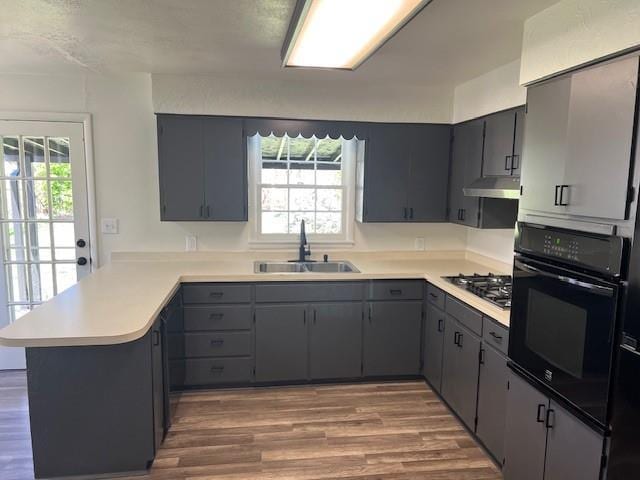 kitchen featuring black oven, a sink, a peninsula, stainless steel gas cooktop, and wood finished floors