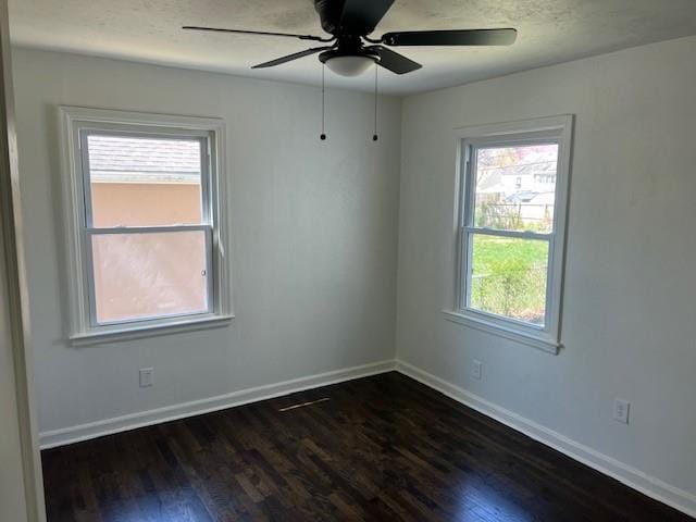 empty room with dark wood-style floors, plenty of natural light, a ceiling fan, and baseboards