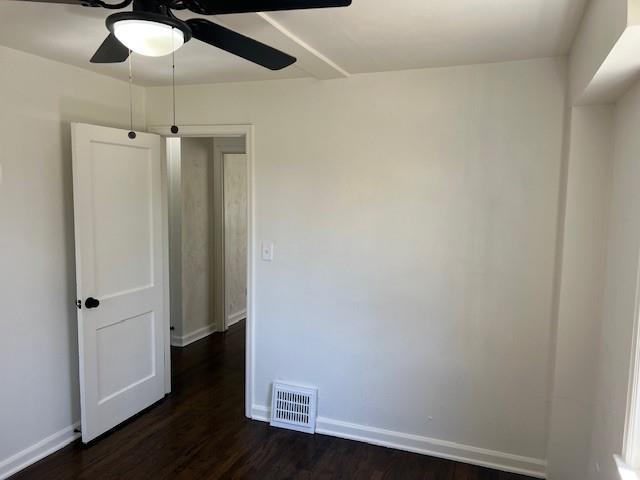 empty room featuring a ceiling fan, dark wood-type flooring, and baseboards