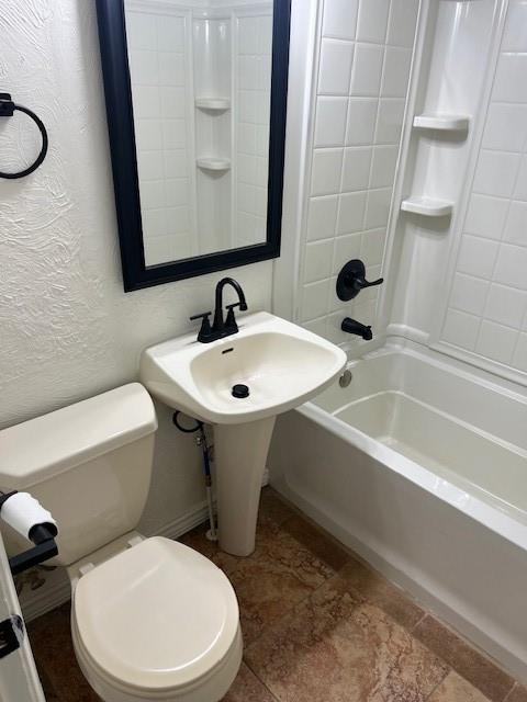 bathroom featuring a textured wall, toilet, and bathing tub / shower combination