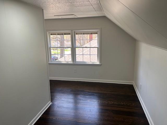 additional living space featuring wood finished floors, vaulted ceiling, and baseboards