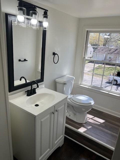 half bathroom featuring toilet, vanity, wood finished floors, and baseboards