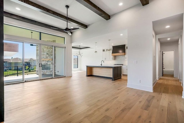 unfurnished living room with beam ceiling, light wood finished floors, baseboards, a sink, and recessed lighting