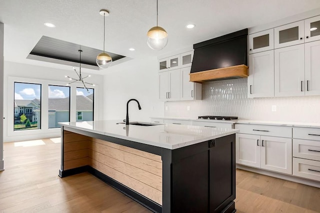 kitchen featuring a sink, a raised ceiling, custom exhaust hood, light wood finished floors, and recessed lighting