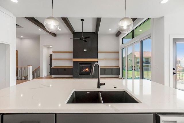 kitchen with a sink, ceiling fan, beamed ceiling, light stone counters, and a fireplace
