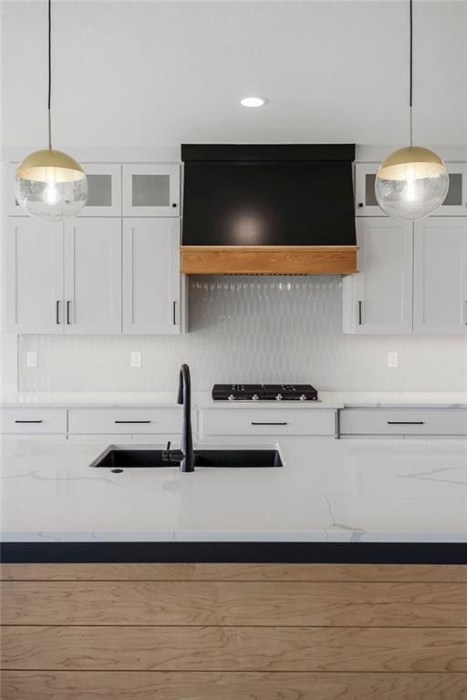 kitchen featuring white cabinets, tasteful backsplash, a sink, decorative light fixtures, and light stone counters