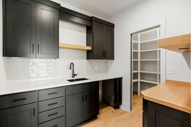 kitchen with a sink, decorative backsplash, light wood-style floors, open shelves, and light countertops