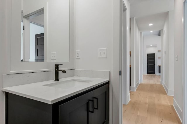 bathroom featuring wood finished floors, vanity, baseboards, and recessed lighting