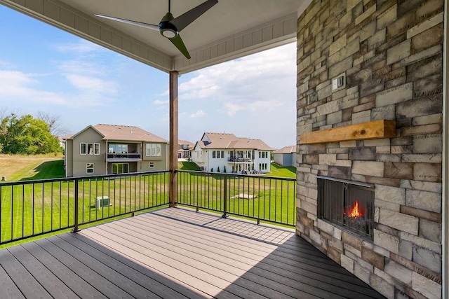 deck with an outdoor stone fireplace, a residential view, a ceiling fan, and a yard