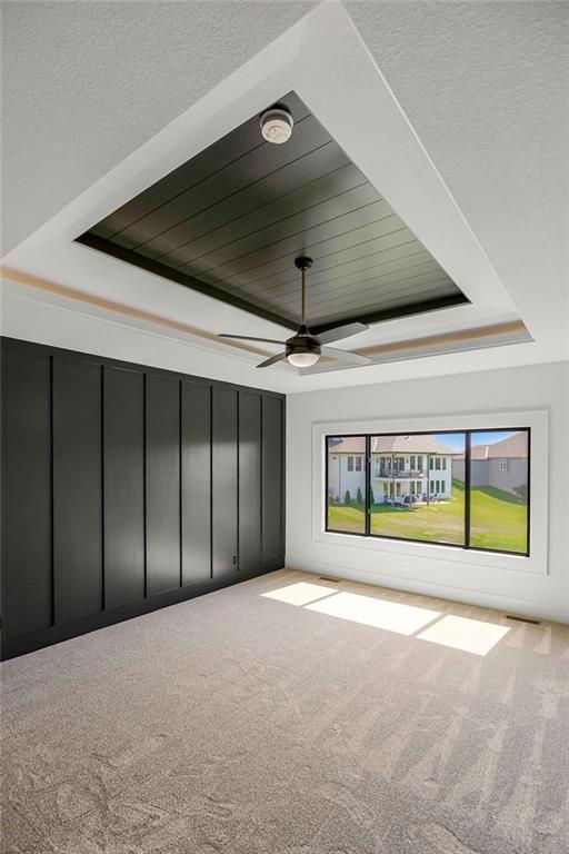carpeted empty room with a tray ceiling, a ceiling fan, and a smoke detector