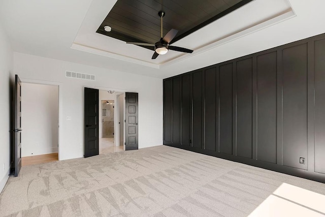 unfurnished bedroom featuring a raised ceiling, light colored carpet, a decorative wall, and ceiling fan
