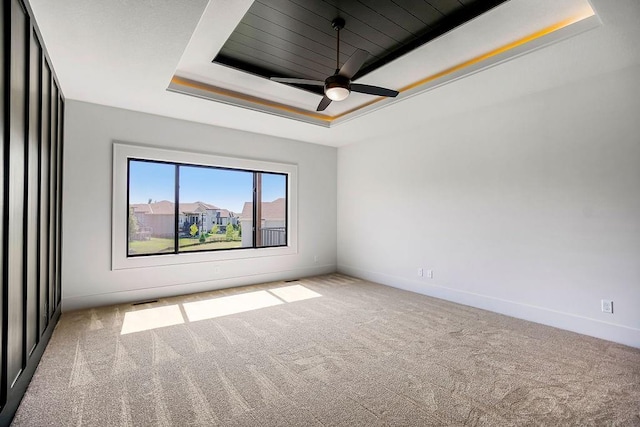 unfurnished room with a raised ceiling, carpet flooring, baseboards, and a ceiling fan