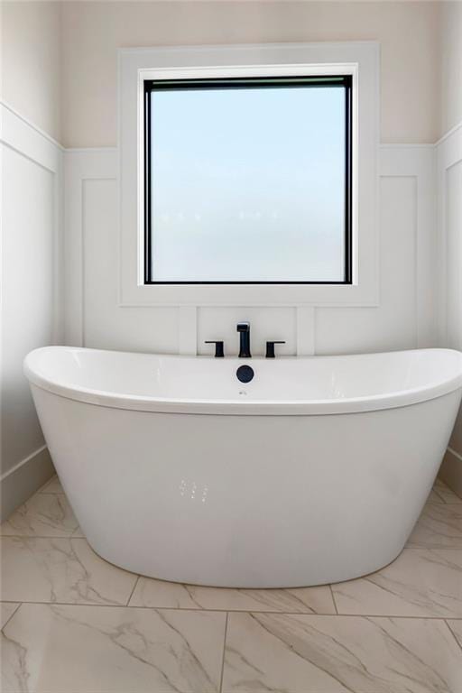 full bath with marble finish floors, healthy amount of natural light, a wainscoted wall, a decorative wall, and a freestanding tub