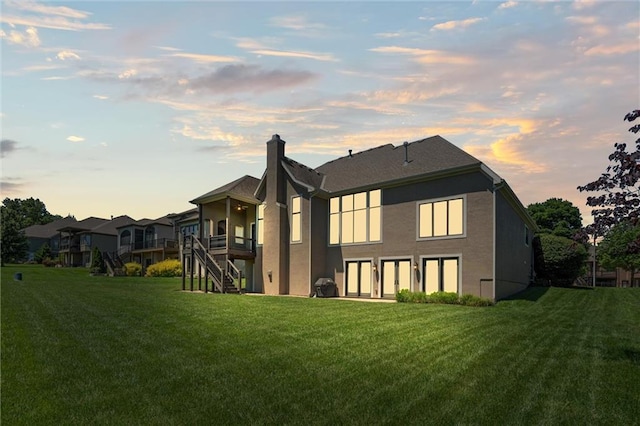 10233 N Prospect Ave, Kansas City, MO 64155 - back of house at dusk with a lawn, a chimney, stucco siding, and stairs
