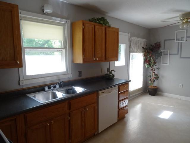 6780 SW County Road 2007th Rd, Rich Hill, MO 64779 - kitchen with white dishwasher, a sink, dark countertops, and brown cabinets