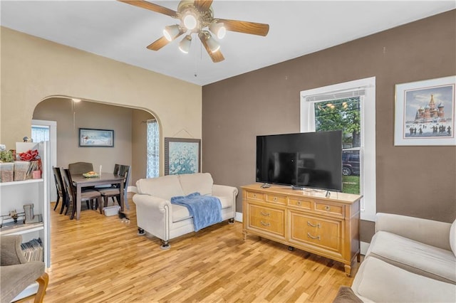 living room featuring arched walkways, light wood finished floors, a ceiling fan, and healthy amount of natural light