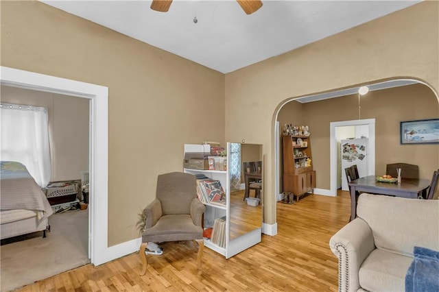 sitting room featuring arched walkways, wood finished floors, a ceiling fan, and baseboards