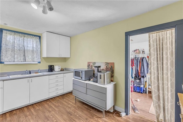 kitchen with stainless steel microwave, a sink, light wood-style floors, white cabinets, and light countertops