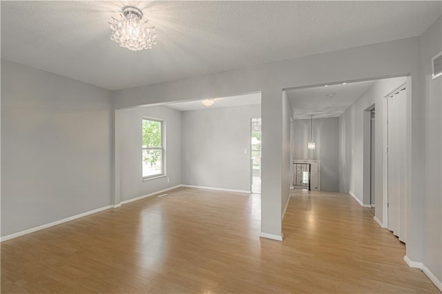 9406 Switzer St, Overland Park, KS 66214 - empty room with light wood-style flooring, a chandelier, baseboards, and a textured ceiling
