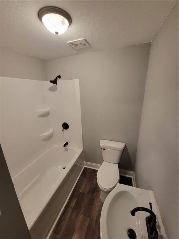 bathroom featuring toilet, wood finished floors, a textured ceiling, a sink, and tub / shower combination