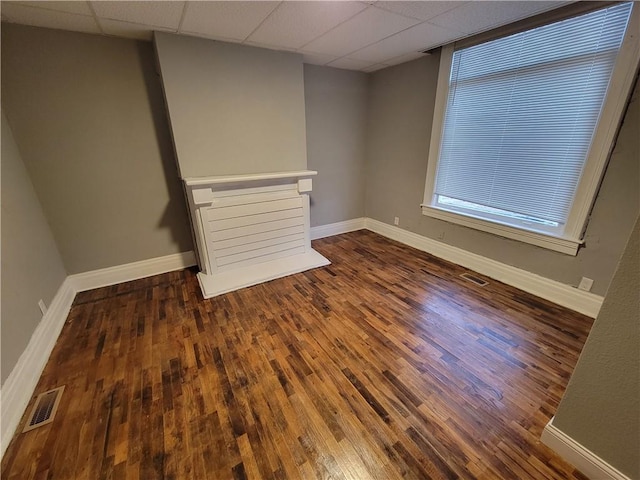 empty room featuring wood finished floors, a paneled ceiling, baseboards, and healthy amount of natural light