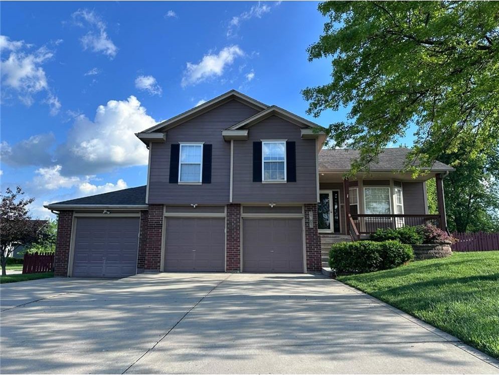 1703 Rolling Rock Rd, Raymore, MO 64083 - split level home with concrete driveway, an attached garage, brick siding, and a porch