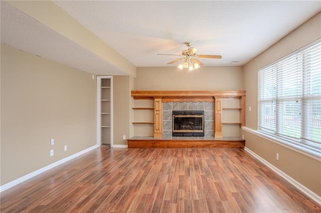 1703 Rolling Rock Rd, Raymore, MO 64083 - unfurnished living room featuring a ceiling fan, wood finished floors, a fireplace, a textured ceiling, and built in shelves