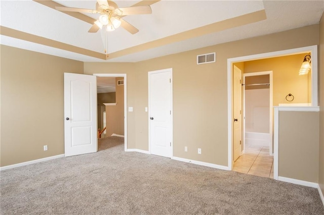1703 Rolling Rock Rd, Raymore, MO 64083 - unfurnished bedroom featuring carpet floors, a tray ceiling, connected bathroom, and a ceiling fan