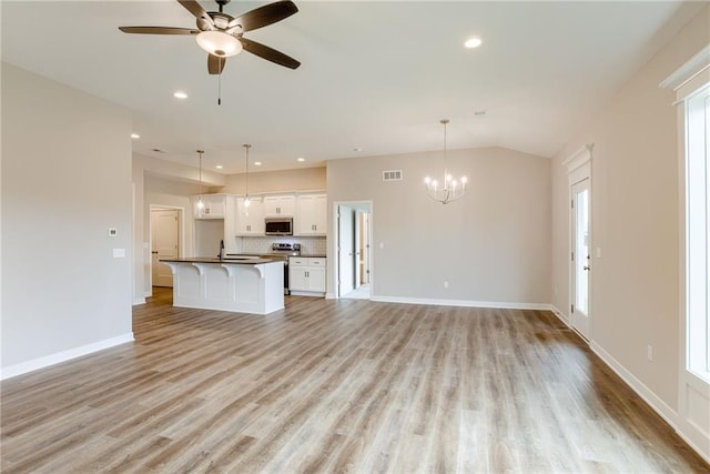 unfurnished living room with a chandelier, light wood finished floors, a ceiling fan, baseboards, and vaulted ceiling