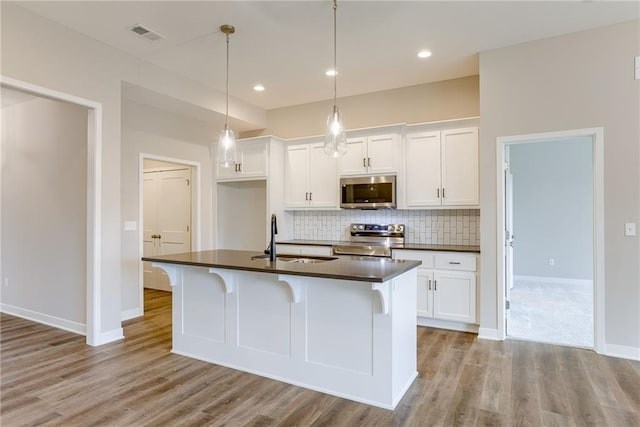 kitchen with a sink, appliances with stainless steel finishes, dark countertops, tasteful backsplash, and light wood-style floors